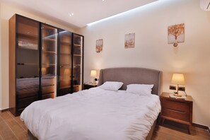 Un dormitorio con una cama grande, un armario, dos mesitas de noche con lámparas, y una obra de arte en la pared.