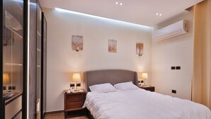A modern hotel room with a large bed, bedside lamps, a nightstand, and a wall-mounted air conditioner.