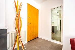 Um corredor com uma porta de madeira, um radiador e um espelho refletindo uma cozinha.