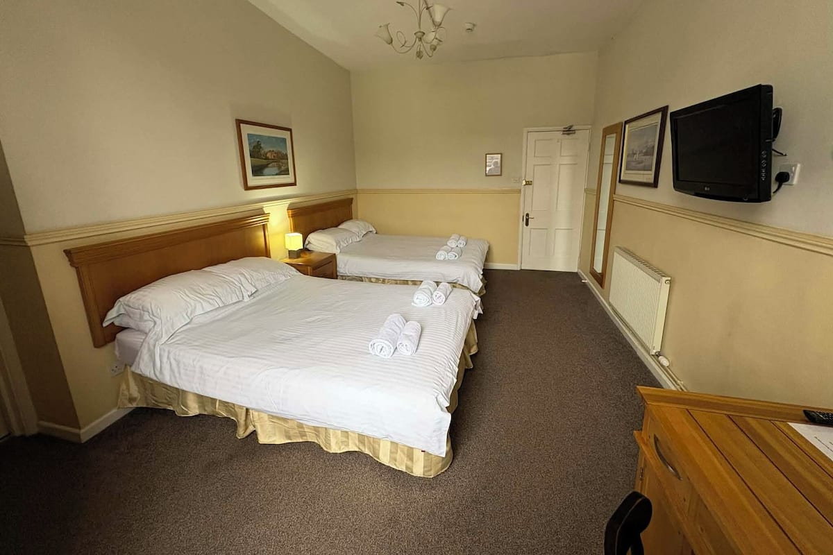 A hotel room with two beds, a television, a door, and a chandelier.