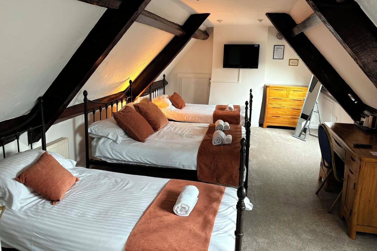 A room with two beds, a wooden desk, a television, and a wooden cabinet.