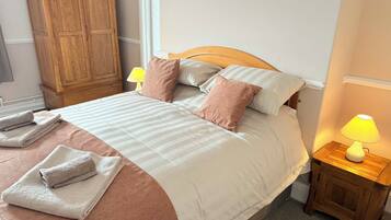 Una cama bien hecha con almohadas, un armario de madera, una lámpara de noche y toallas dobladas.