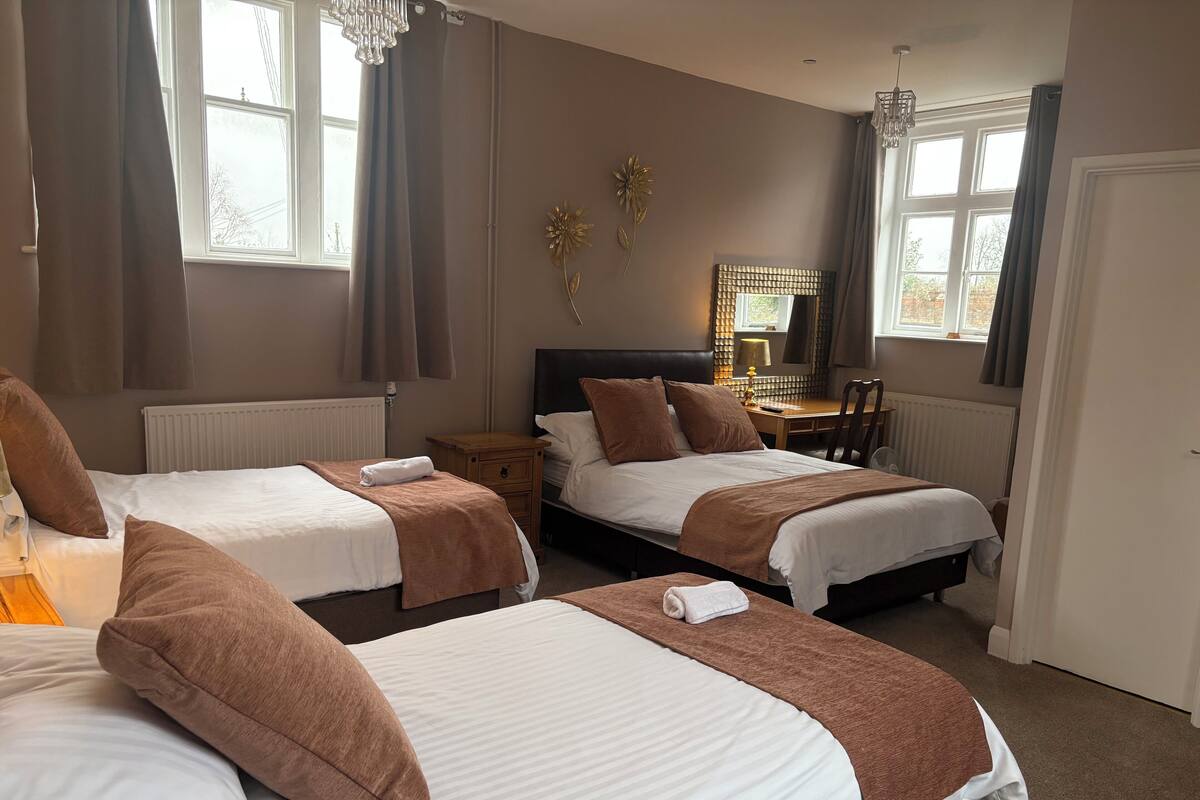 A hotel room with two beds, a desk, a chair, and a window with curtains.