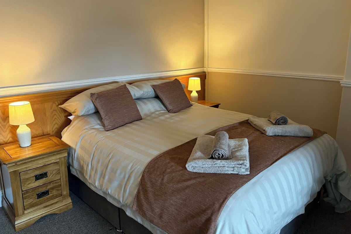 A neatly made bed with pillows, a bedside lamp, and a folded towel on the nightstand.