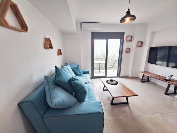 A modern living room with a sofa, a coffee table, a TV, and a balcony. - Viki's Sea View Apartment (Lefkada)