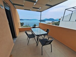 Un balcon avec une table et des chaises, une vue sur la mer et les montagnes, et un bâtiment à la façade blanche.