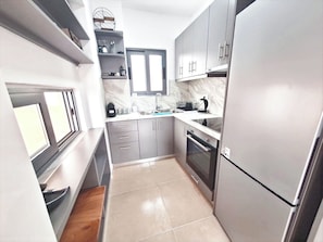 A compact kitchen with grey cabinets, a built-in oven, and a window above the sink. - Viki's Sea View Apartment (Lefkada)