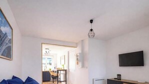 A room with a bed, a TV, a painting, and a door leading to a kitchen. - L'Instant Renouveau - Park & animals (Le Mans)