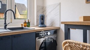A modern kitchen with a built-in dishwasher, a coffee maker, and a window with a view of a house. - L'Instant Renouveau - Park & animals (Le Mans)