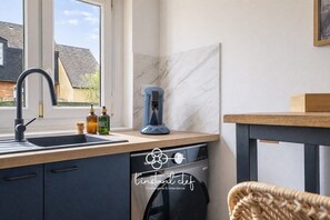 Une cuisine moderne équipée d’un lave-vaisselle intégré, d’une machine à café et d’une fenêtre donnant sur une maison.