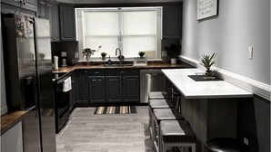 A modern kitchen with dark cabinets, a stainless steel refrigerator, a built-in oven, a sink, and a bar area with stools. - Cozy 2-bedroom apartment in beautiful Ewing Township with AC (Ewing Township)