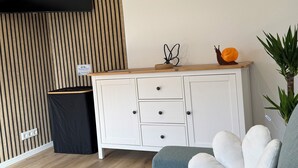 Ett modernt vardagsrum med en soffa, en tv som är monterad på väggen, ett träskåp och en liten papperskorg.