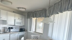 Une cuisine avec des meubles blancs, un four à micro-ondes, une cuisinière, une machine à café et une table à manger avec des chaises.