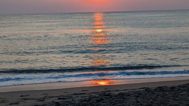 Une plage avec des vagues, un coucher de soleil et un ciel dégagé.