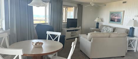 Et hotelværelse med et spisebord, stole, en sofa, et fjernsyn, en lampe og et maleri på væggen.