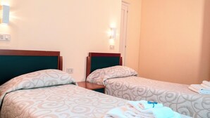 Een hotelkamer met twee bedden, elk voorzien van beddengoed met een patroon, nachtlampjes en een netjes gevouwen handdoek op het rechterbed.