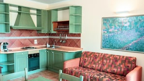 Een kleine keuken met groene kastjes, een spoelbak en een zithoek met een tafel en een bank.