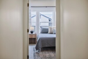 A bedroom with a bed, nightstand, lamp, and a view of the outside. - ¡SocialHaus! Sleeps 16! 5 mins to Gainbridge (Indianapolis)