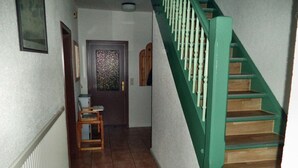 Una scala con corrimano verdi, una porta in legno con pannello in vetro decorato e una piccola sedia di legno.