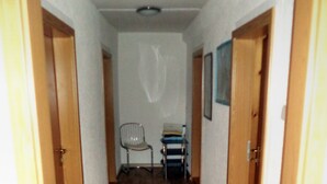 Un corridoio con pavimento in legno, una sedia, un tavolino con dei libri e una porta alla destra.