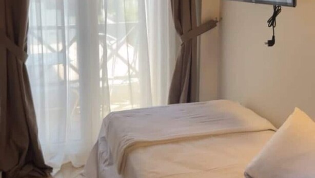 A bedroom with a bed, curtains, a TV mounted on the wall, and a tiled floor. - Mersea standard apt - cosy holidays in Kourouta (Kourouta)
