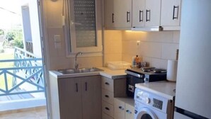 A compact kitchen with a washing machine, a sink, and a window with blinds. - Mersea standard apt - cosy holidays in Kourouta (Kourouta)