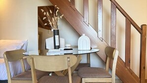 A dining area with a wooden table and chairs, a vase with dried flowers, and a staircase with wooden railings. - Mersea standard apt - cosy holidays in Kourouta (Kourouta)