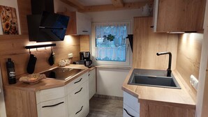 A kitchen with wooden cabinets, a window with a view, a coffee maker, and a sink. - Cozy wooden cottage under the small Zschirnstein (Kleingießhübel)