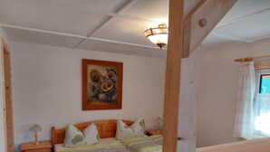 A bedroom with a wooden bed, a nightstand with a lamp, a painting on the wall, and a window with curtains. - Cozy wooden cottage under the small Zschirnstein (Kleingießhübel)