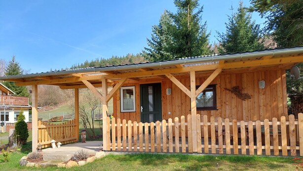 A wooden cabin with a porch, a fenced yard, and a mountain backdrop. - Cozy wooden cottage under the small Zschirnstein (Kleingießhübel)