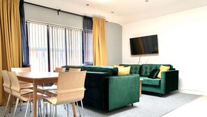Una sala de estar moderna con un sofá verde, una mesa de comedor de madera con sillas y un televisor de pantalla plana montado en la pared.