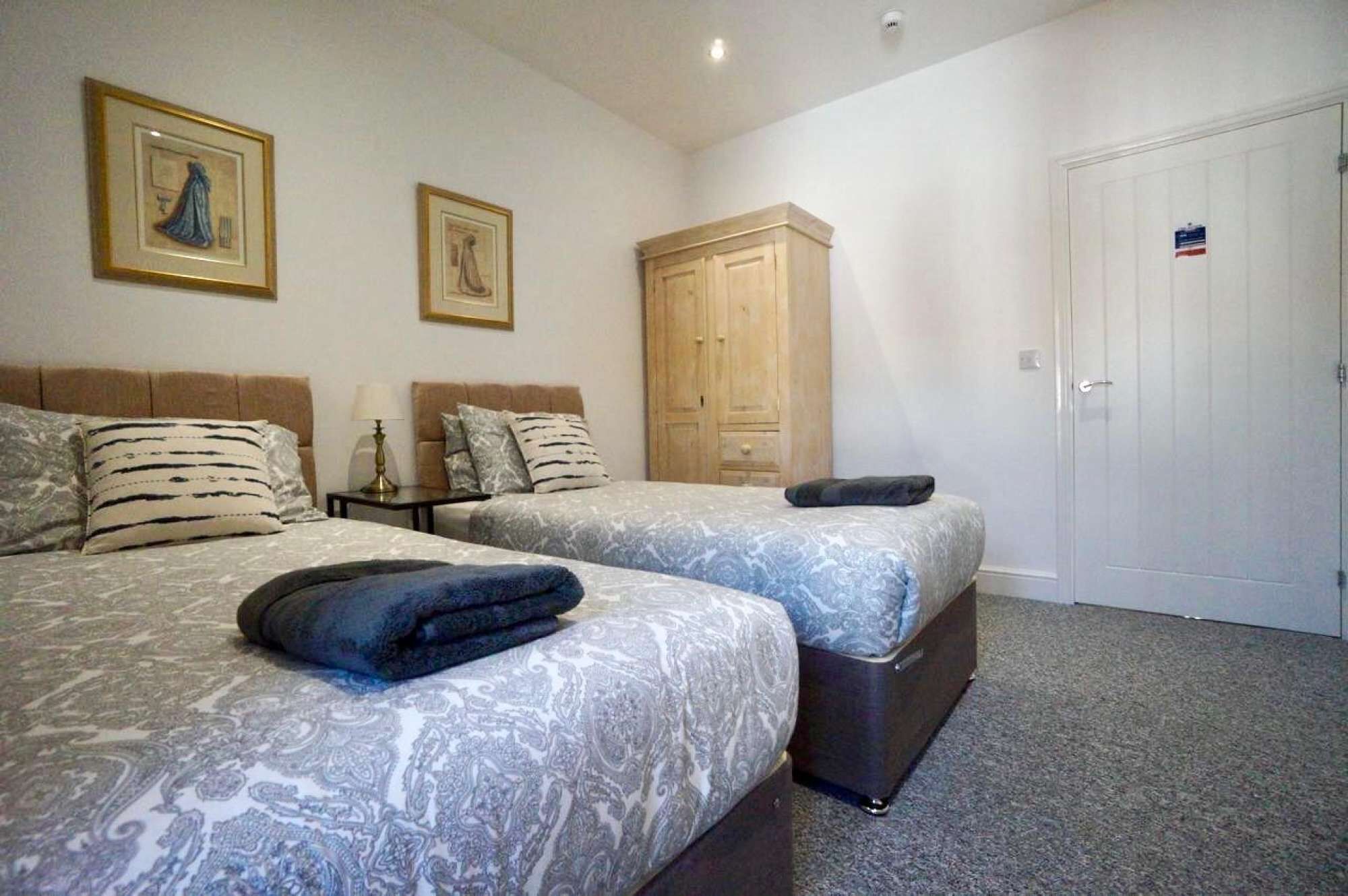 A hotel room with two beds, a wardrobe, a door with a sign, and two framed pictures on the wall.