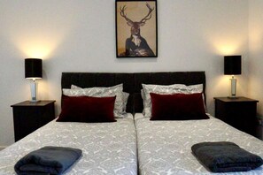 A double bed with patterned bedding, two bedside tables with lamps, and a deer-themed artwork on the wall. - B - Delux 2-bedroom apartment in the center of Thatcham (Thatcham)