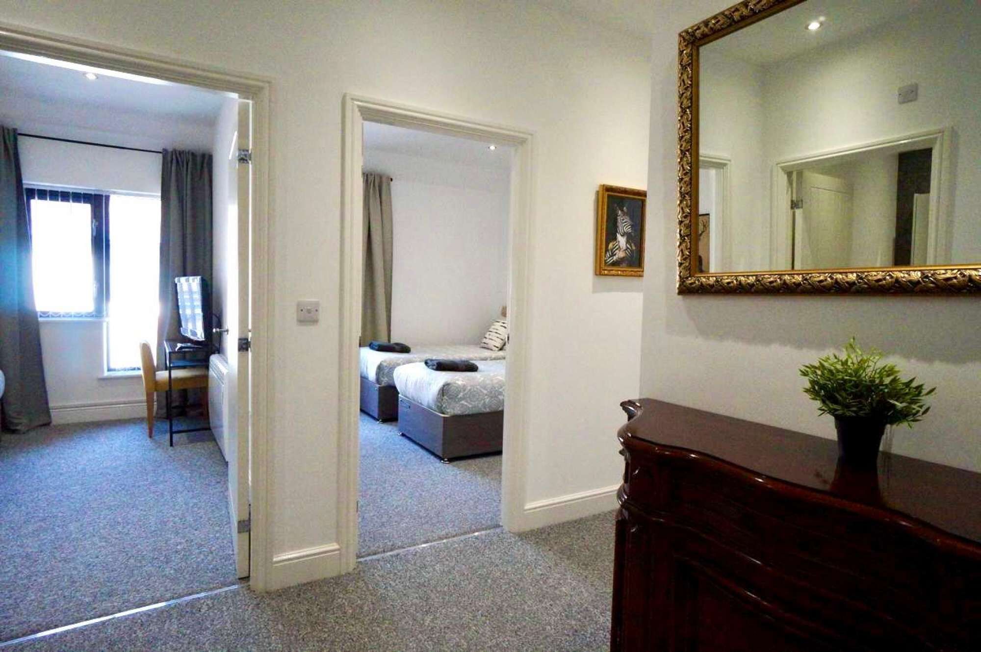 Une chambre d’hôtel avec un lit, un bureau, une chaise, un miroir et une plante.