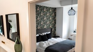 A bedroom with a bed, a dresser, a mirror, a vase, a wall with floral wallpaper, a bedside table, and a hanging light fixture. - Modern apartment in the heart of Offenbach (Offenbach am Main)