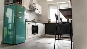A kitchen with a teal refrigerator, white cabinets, a black countertop, and a black chair. - Modern apartment in the heart of Offenbach (Offenbach am Main)