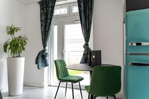 Een moderne kamer met een eettafel, stoelen, een potplant en een blauwgroene koelkast.