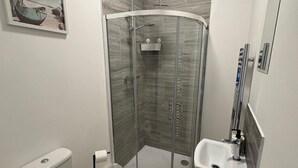 Ein Badezimmer mit Eckausstattung, einer Duschkabine, einer Toilette und einem Waschbecken.