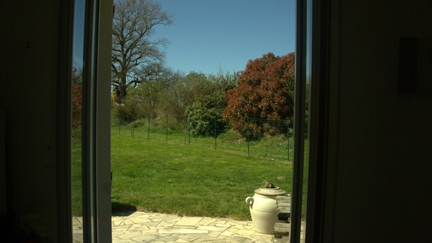 A patio area with a stone floor, a large white urn, and a view of a grassy yard with trees and a fence.
