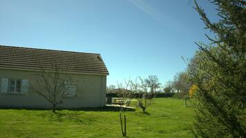 Une maison avec un toit en tuiles, une pelouse et un petit arbre devant.