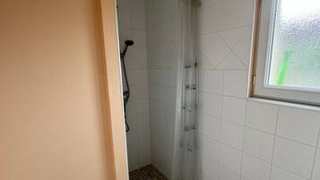 A bathroom with a shower, tiled floor, a radiator, and a window.