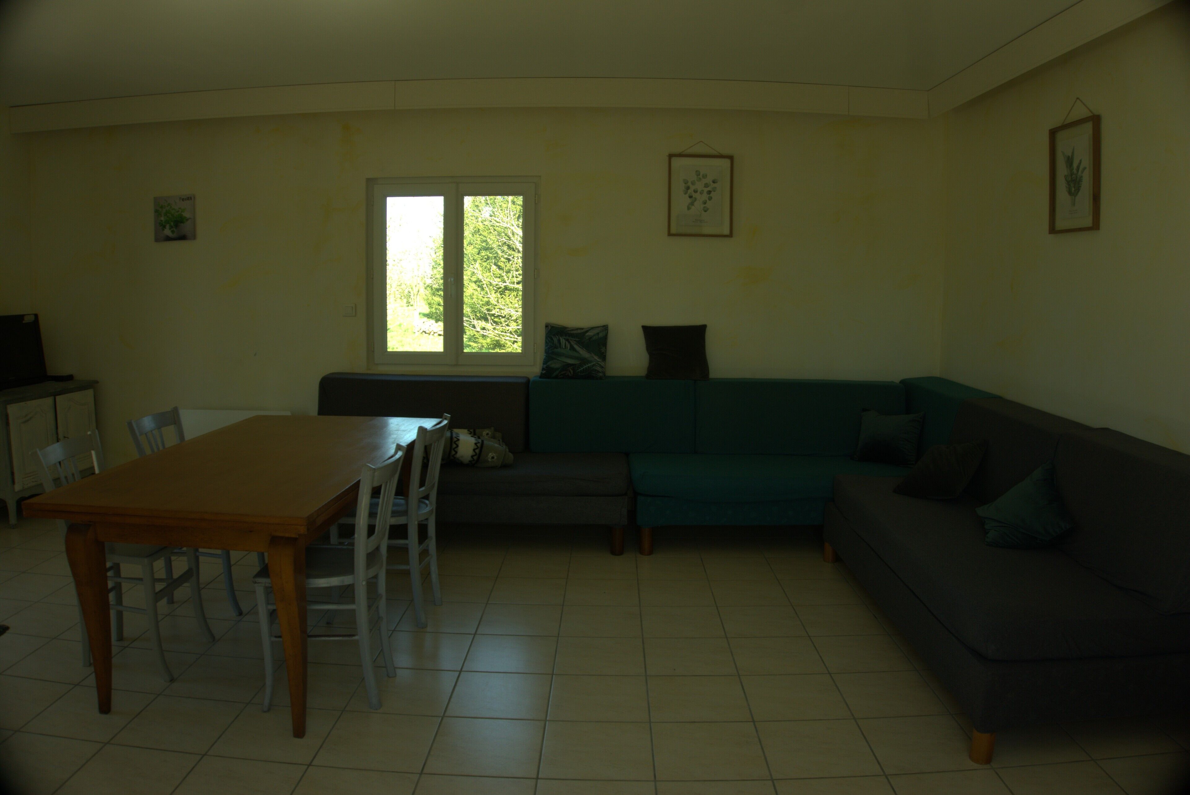 A living room with a wooden table, chairs, a sofa, and a window.