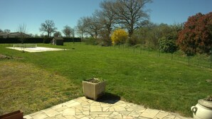 A backyard with a stone patio, a small trash bin, and a fenced area with trees.
