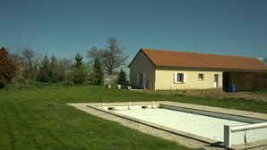 A building with a red roof, a paved area with a white border, and a grassy field with trees.