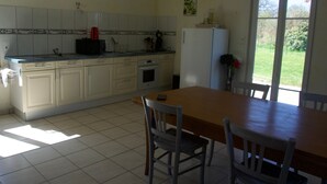 A kitchen with a dining table and chairs, a refrigerator, and a window with a view of greenery.