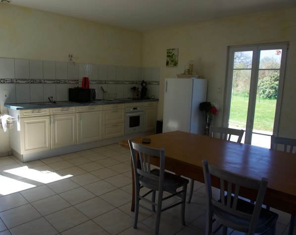 A kitchen with a dining table and chairs, a refrigerator, and a window with a view of greenery.