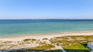 Une vue sur la plage, avec un ciel dégagé, une plage de sable et des zones herbeuses.