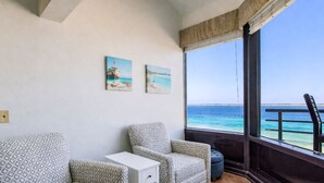 Un balcon avec deux chaises à motifs, une petite table et deux tableaux représentant des paysages côtiers.