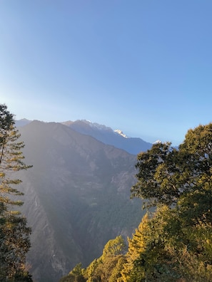 A mountainous landscape with dense forest in the foreground and distant snow-capped peaks under a clear sky.