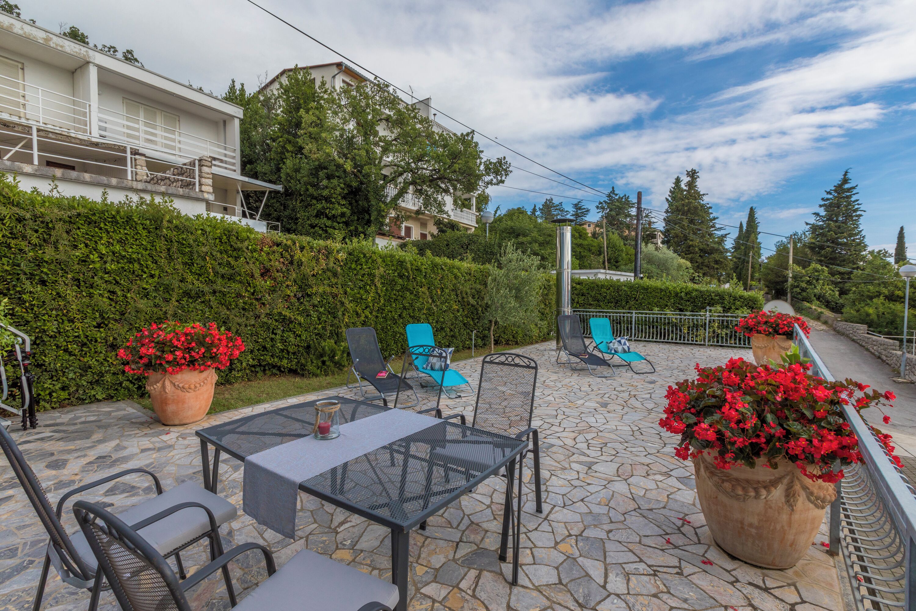 An outdoor patio with stone flooring, metal furniture, and potted plants.